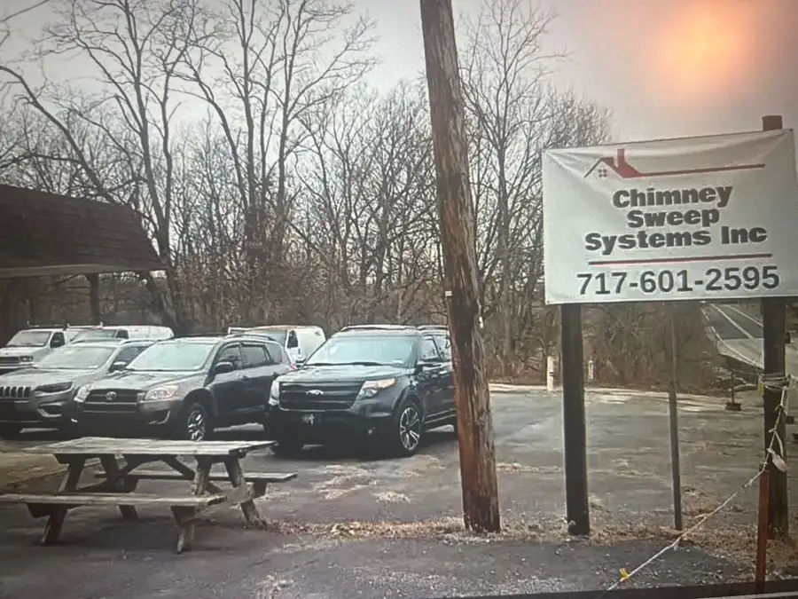 Roadside sign reading Chimney Sweep Systems Inc with the office phone number, cars parked behind it