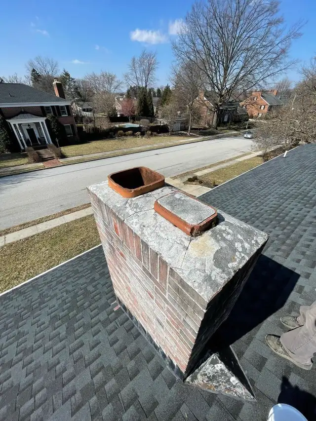 Two terracotta flue tiles standing above a worn chimney crown on a shingle roof
